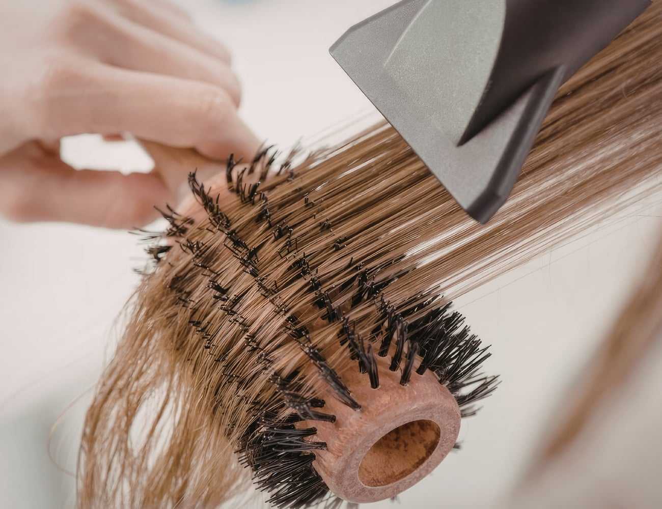 A person uses a round brush and blow dryer to style long hair.