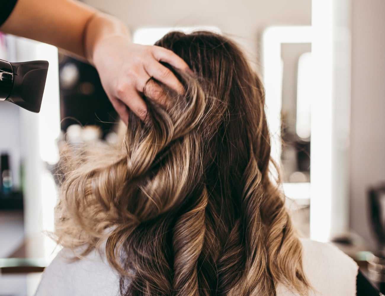 Hair stylist curling woman's long hair in a salon with a blow dryer and hand brushing through it.